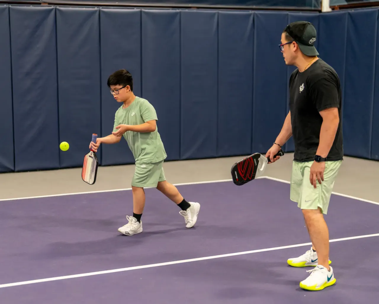 A dad and his young son casually rallying together on the court