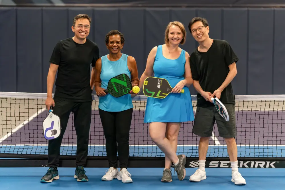 A diverse group of players smiling together at the net with paddles