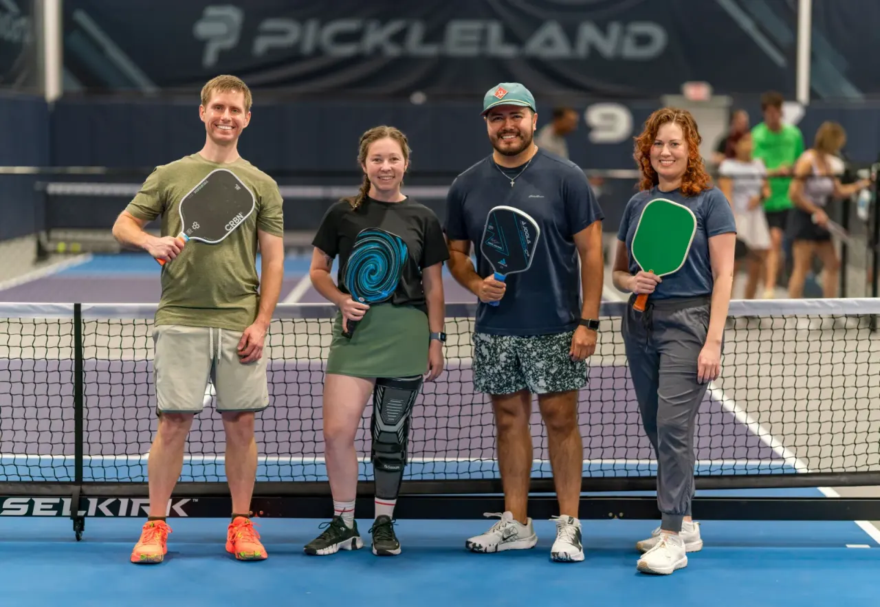 Group of adult pickleball players gathered at the net for a social photo
