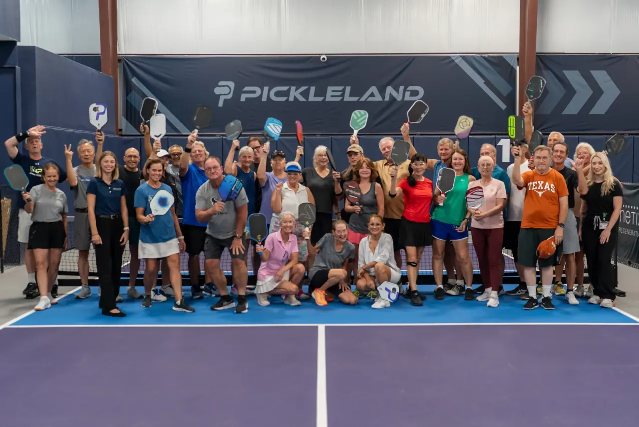 Large community group holding paddles up on a Pickleland court