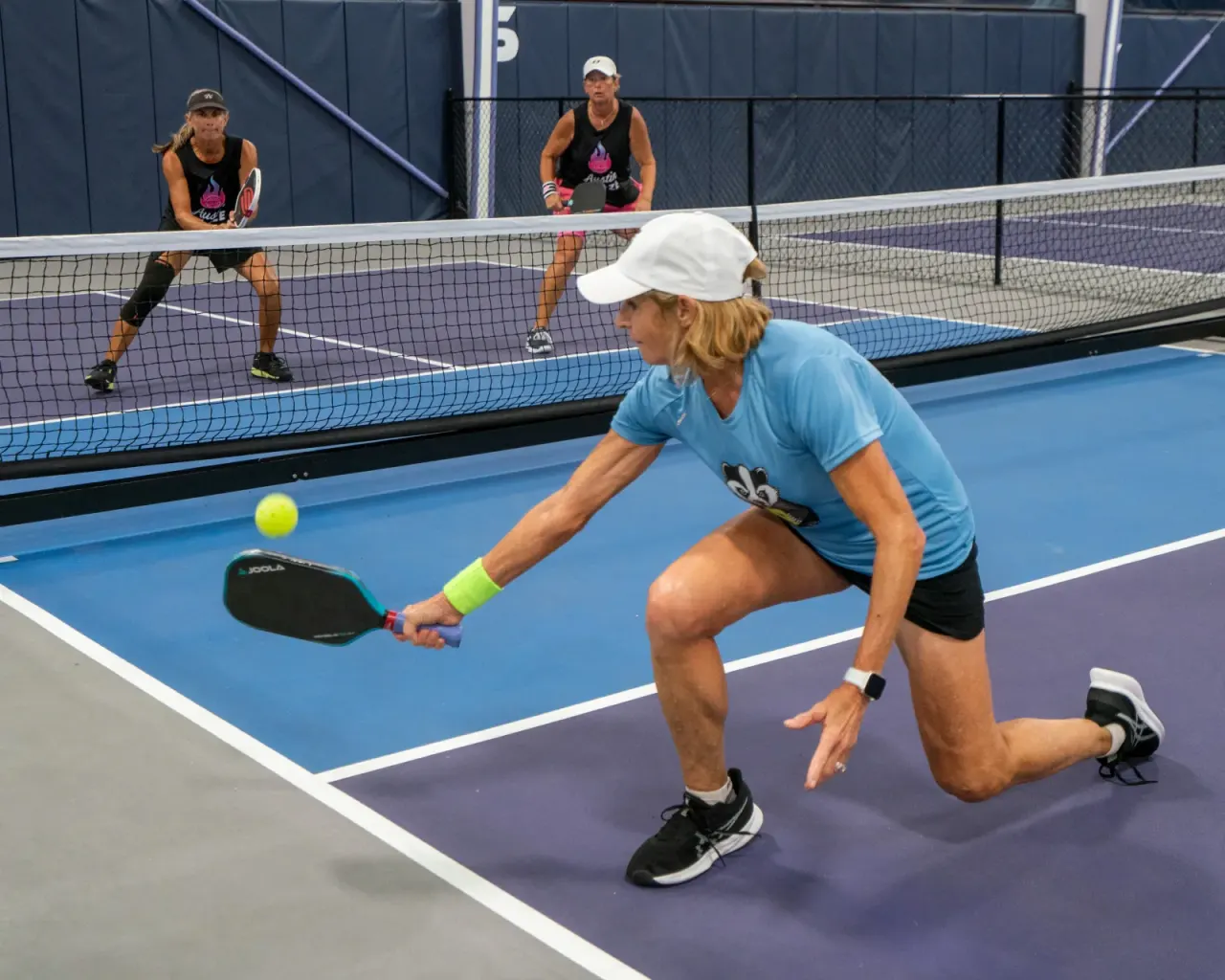 A woman lunging for a dink during indoor pickleball play