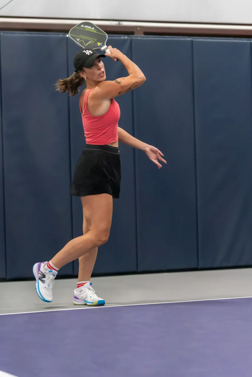 A woman leaps for an overhead smash during an athletic pickleball rally