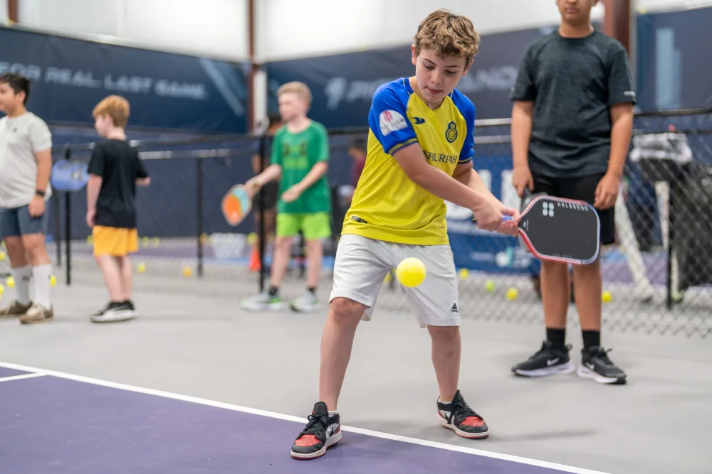 Young player in a yellow jersey rallying at a Pickleland junior clinic