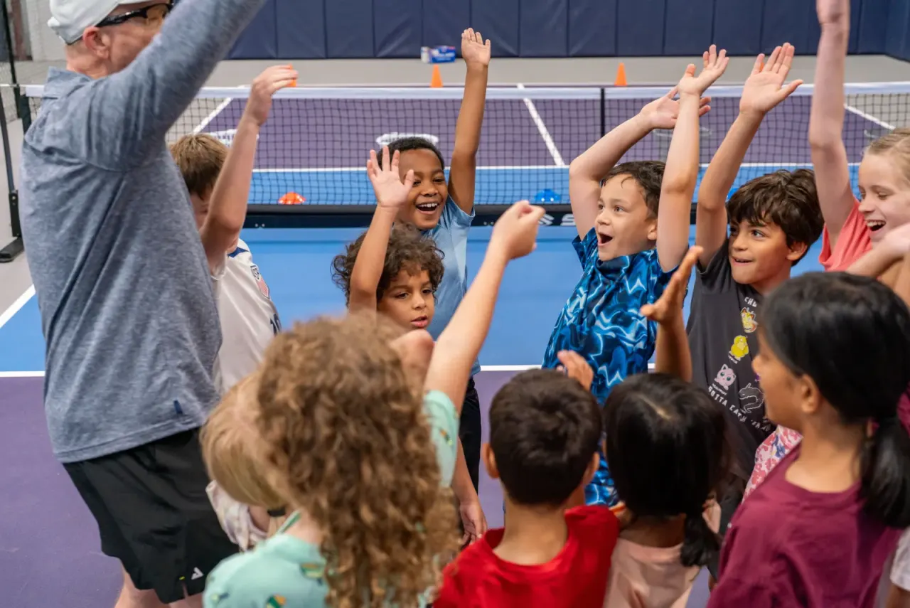 Coach and young kids cheer with hands up at a clinic