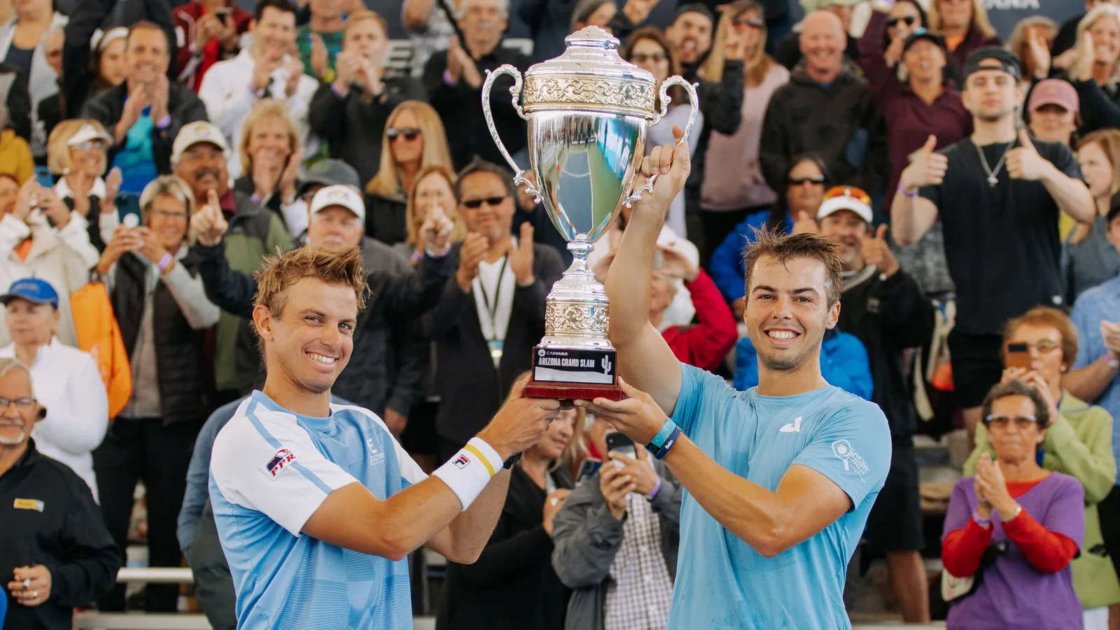 Ben Johns and his brother Collin Johns raise the Arizona Grand Slam trophy in front of a cheering crowd, February 2023