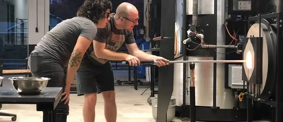 A student shaping a molten glass piece during a glassblowing class at Ghost Pepper Glass