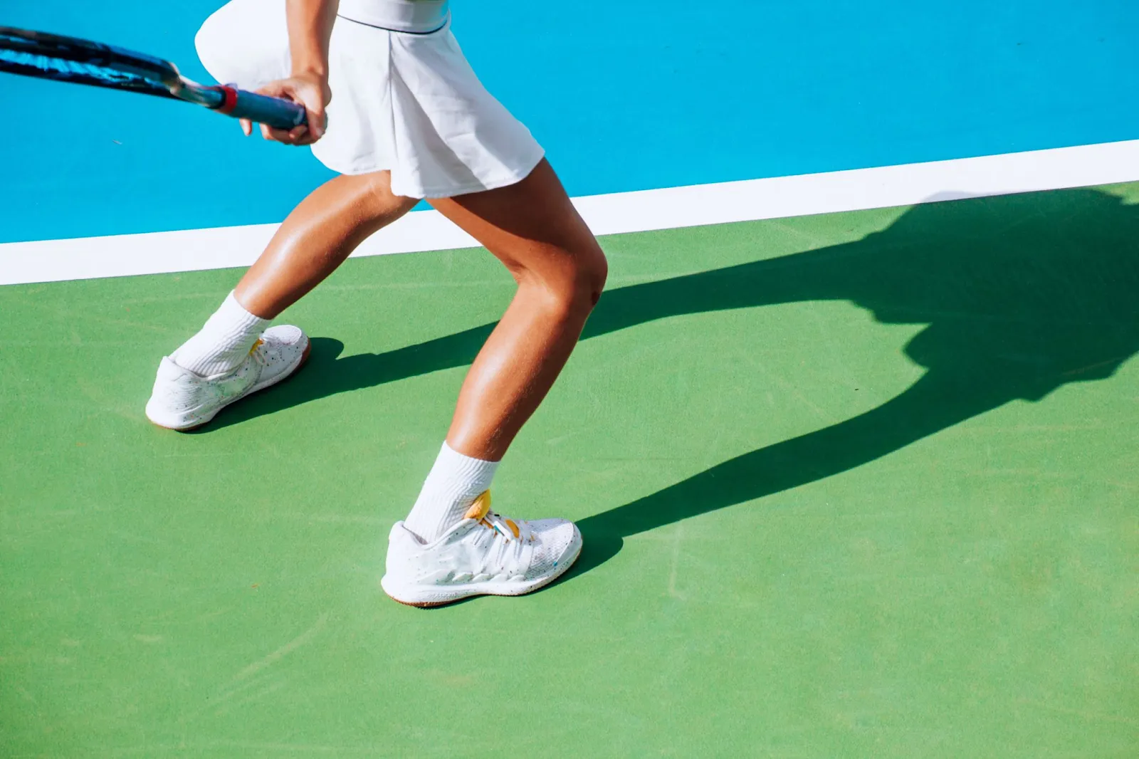 Pickleball player in a low athletic stance wearing supportive white court shoes on a hard court