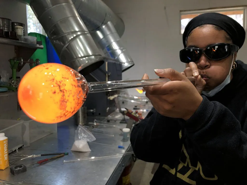 Artisan shaping molten glass with tools during a glassblowing class